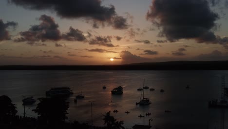 dolly in aerial shot of the alligator beach, a river in cabedelo, paraiba, brazil, near the coastal capital city of joao pessoa, with tour boats watching the sunset as a man plays the saxophone below