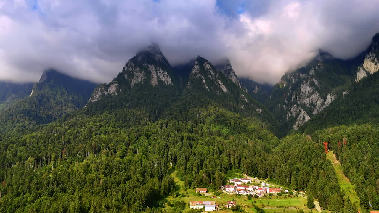 Tops of the mountains are hidden by the dramatic cloudscape. Evergreen pine tree woods cover the slopes of the rocks. The Bucegi Mountains of the Southern Carpathians, Romania