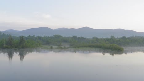 Aerial-gliding-over-lake-shoreline-tranquil-morning-fog-mountains-in-distance