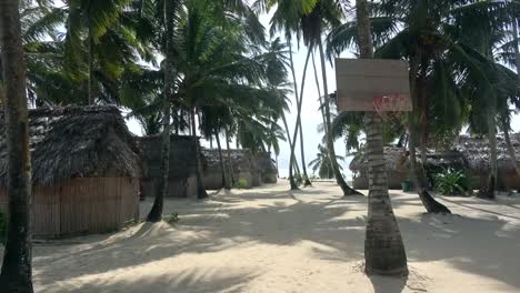 Tropical-vacation-beach-view-with-huts-and-wind-in-palm-trees