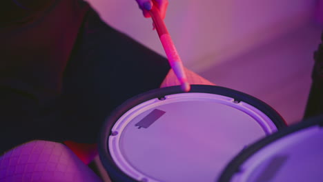 leg view of woman in fishnet pantyhose striking electronic drum pad and kick sensor during practice under neon pink studio lighting, showcasing rhythmic motion and focused energy