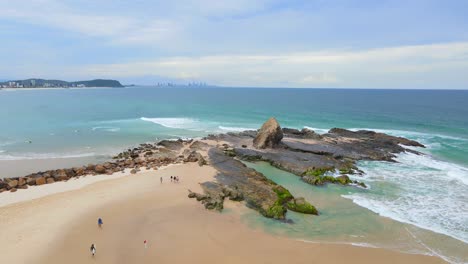 gente caminando hacia la formación rocosa en la playa de currumbin - currumbin rock, qld, australia