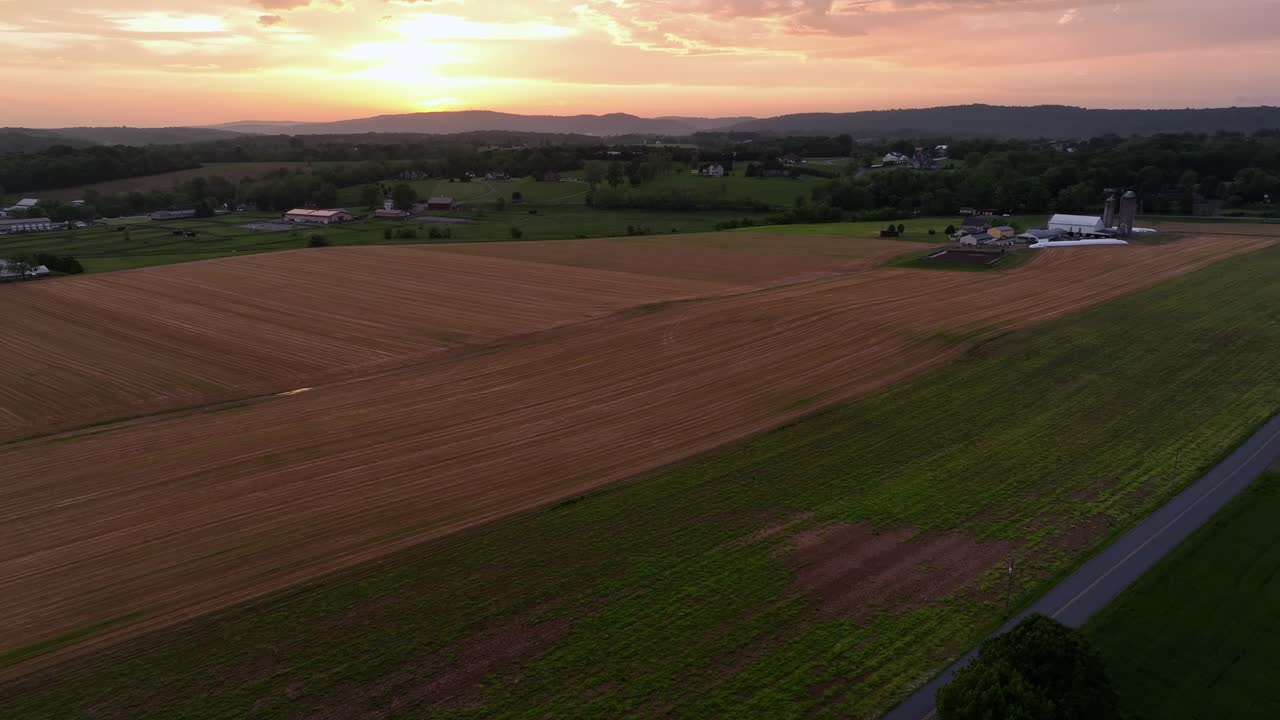 Quiet american farmland and cropland during golden sunset. Aerial wide shot. Farmstead with mountain range in Background. Midwest, America.
