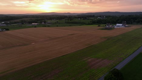 quiet american farmland and cropland during golden sunset. aerial wide shot. farmstead with mountain range in background. midwest, america.