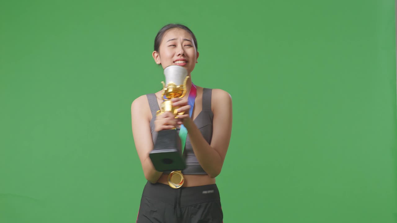 금메달을  아시아 여성이 금 트로피에서 노래를 부르고 스튜디오의 녹색 화면 배경에서 첫 번째 우승자로 우승을 축하합니다.