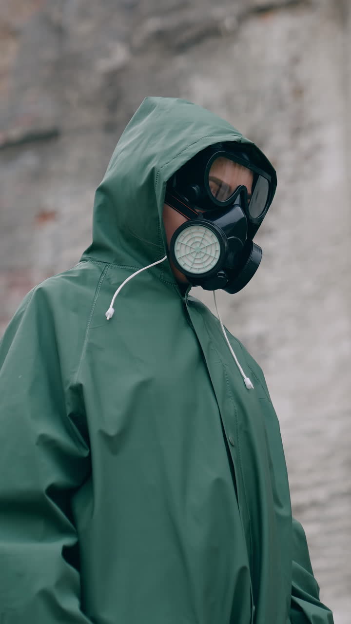 Unrecognizable person in safety suit and respirator. Human wearing hazmat suit looking for somebody on the background of destroyed building. Chemical attack. Vertical video