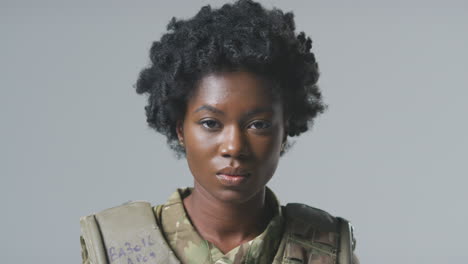 studio portrait of serious young female soldier in military uniform against plain background