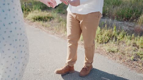 couple holding hands, with focus on their joined hands, standing in a sunny outdoor setting