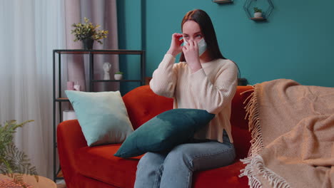 Young-Caucasian-sick-woman-wearing-medical-protection-mask-sitting-in-living-room-looking-at-camera