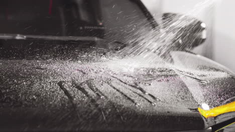 a mesmerizing cascade of water droplets dances across a sleek black car hood in slow motion