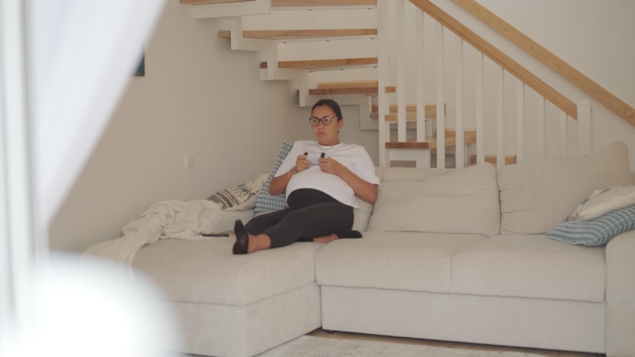 una hermosa mujer embarazada sentada cómodamente en casa, disfrutando de videojuegos en una consola de televisión. la escena mezcla relajación, entretenimiento moderno y maternidad en un entorno acogedor