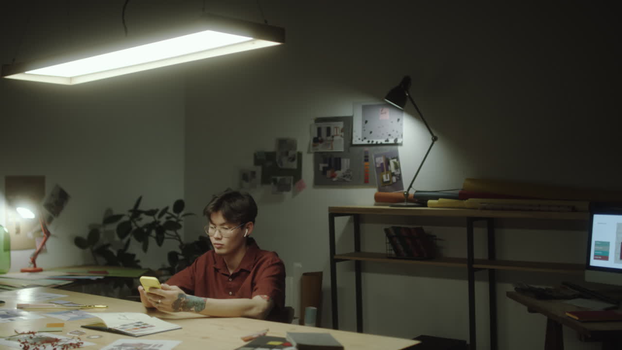 Young person using a smartphone at a desk in a dimly lit office