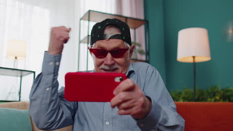 Worried-funny-senior-old-grandfather-man-playing-shooter-online-video-games-on-mobile-phone-at-home