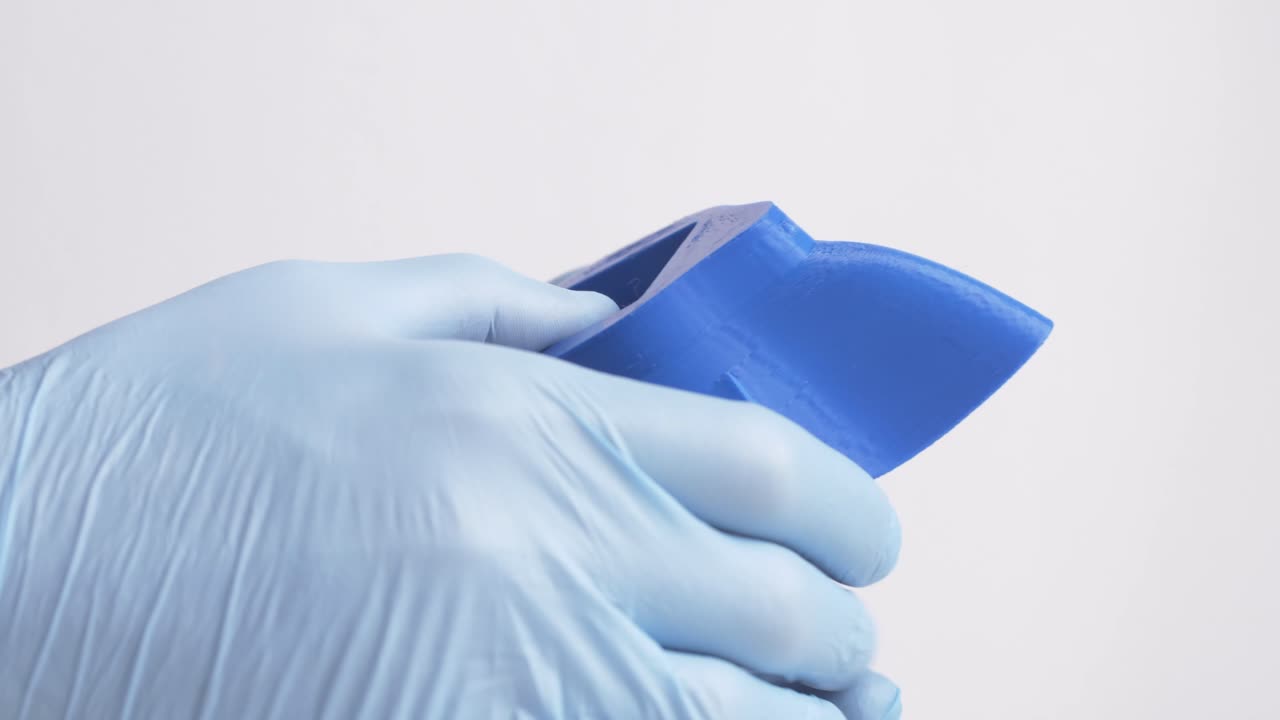 Male wearing surgical gloves handling a 3D printed plastic mask during the COVID-19 pandemic