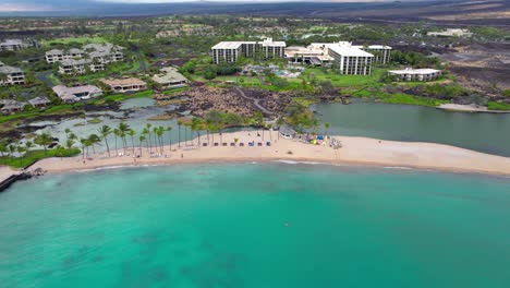 Retroceso-Aéreo-Sobre-La-Bahía-De-Anaehoomalu,-Hawaii-Hermosa-Playa-Tropical-Con-Aguas-Azules-Claras