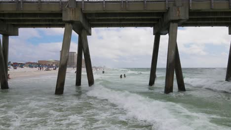 Epic-Aerial-Shot-Flying-Under-Wooden-Pier-by-Sandy-Ocean-Beach-in-Florida