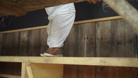 Toddler-boy-walks-left-along-wooden-bench-in-hut,-low-angle,-close-up