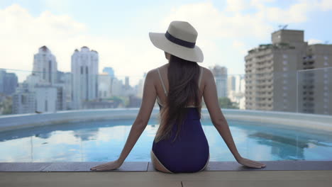 woman sitting on pools edge looking over city sky line