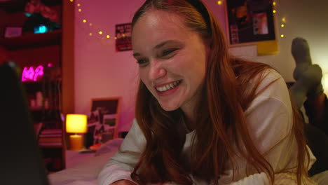 happy young woman laughing while using her laptop in bed