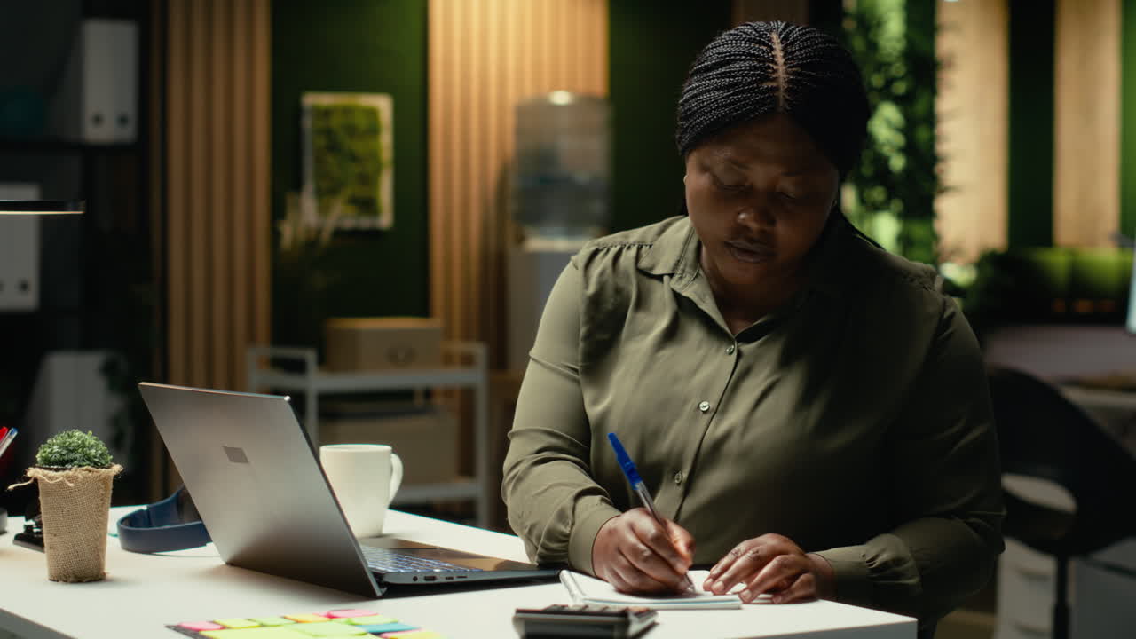 Black analyst documenting essential ideas on paper and reading on laptop