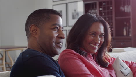 close up de una pareja afroamericana de mediana edad sentada en el sofá en su sala de estar viendo la televisión juntos