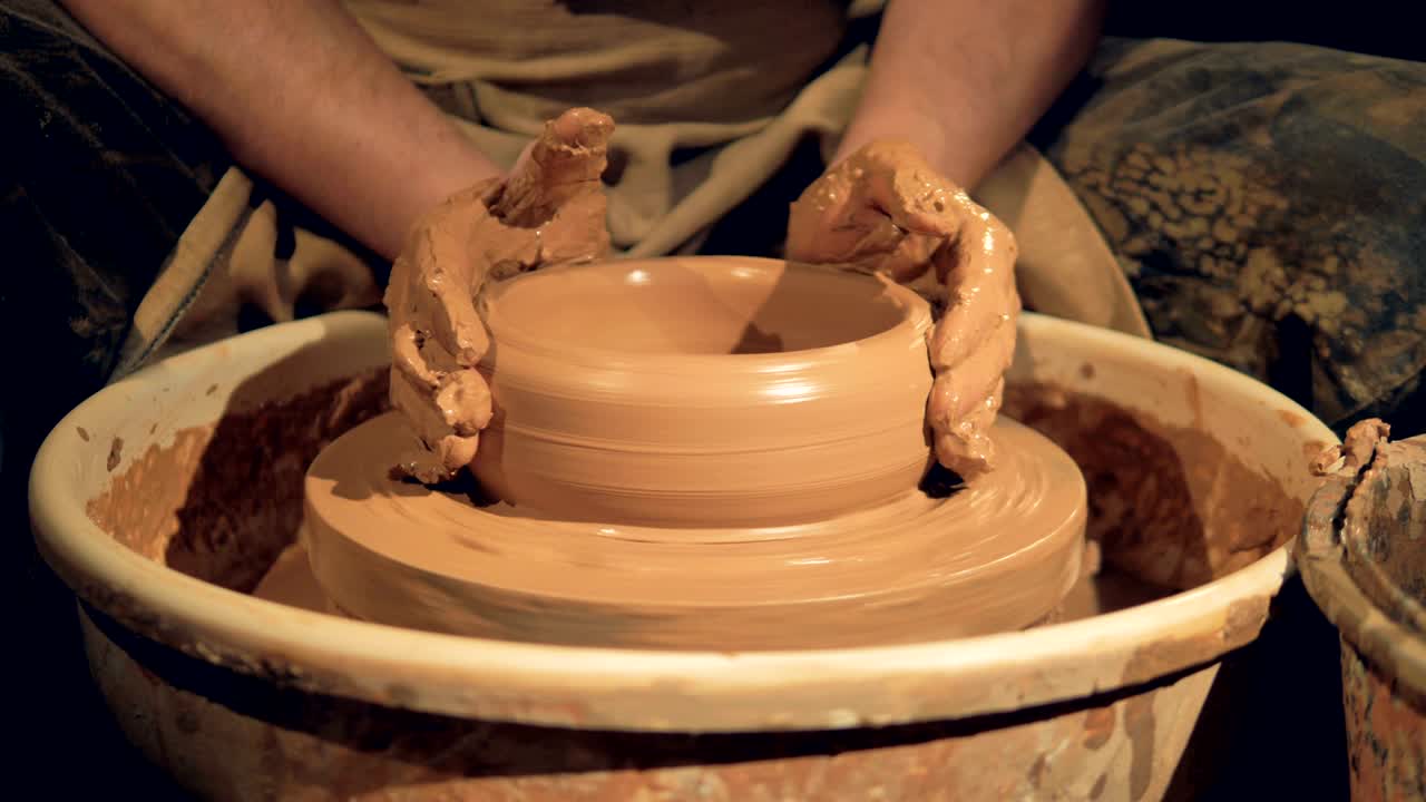 A potter shapes a basic shallow bowl on a wheel.