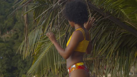 a natural hair model walks on the beach next to palm trees in a sexy bikini