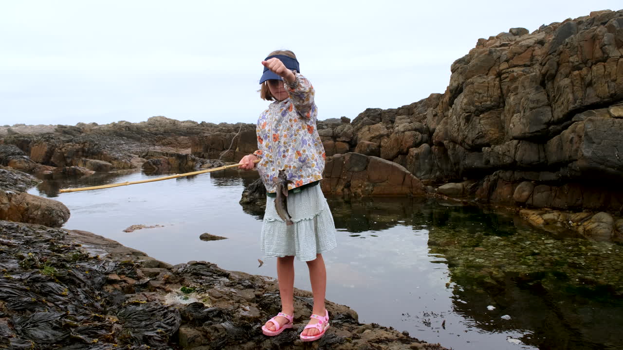 niña con caña de pesca de bambú sostiene un pez clipfish junto a rockpool en la costa
