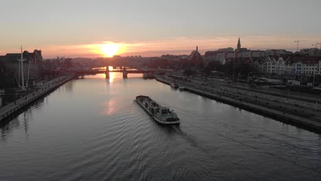 Imágenes-Aéreas-De-Un-Buque-De-Carga-En-El-Río-De-La-Ciudad,-Hermosa-Puesta-De-Sol