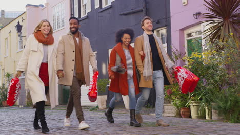 two multi-cultural couples arm in arm as they walk along cobbled mews street on visit to city in autumn or winter carrying sale shopping bags - shot in slow motion