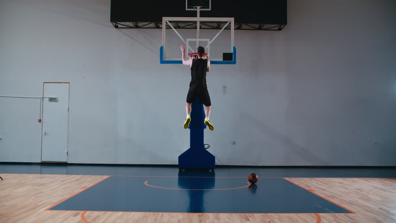 Focused determined sportsman doing pull ups on a basketball court indoors. 4K UHD
