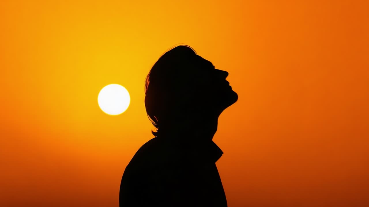 A Serene Sunset Silhouette: Capturing the Tranquility of a Man’s Profile Against a Vibrant Orange Sky with a Setting Sun Illuminating the Scene