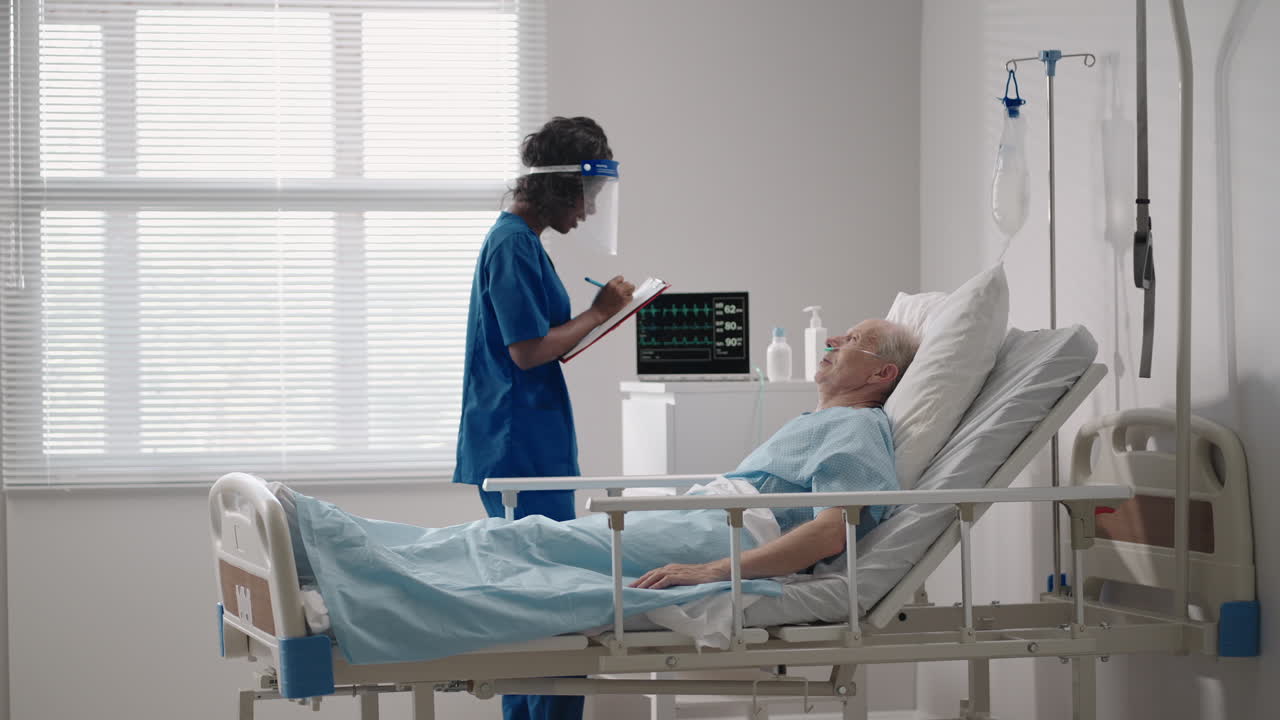 una mujer negra cardióloga está hablando con un anciano paciente acostado en una cama de hospital discutiendo la rehabilitación después de la recuperación. un neurólogo de enfermedades infecciosas discute una estrategia de tratamiento