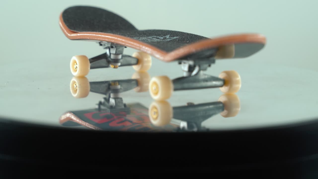 una hermosa y detallada toma de primer plano de un mini patineta, pequeñas ruedas blancas, fingerboard en un soporte giratorio de 360, reflejo brillante en el espejo, iluminación profesional, vídeo cinematográfico 4k inclinado hacia abajo