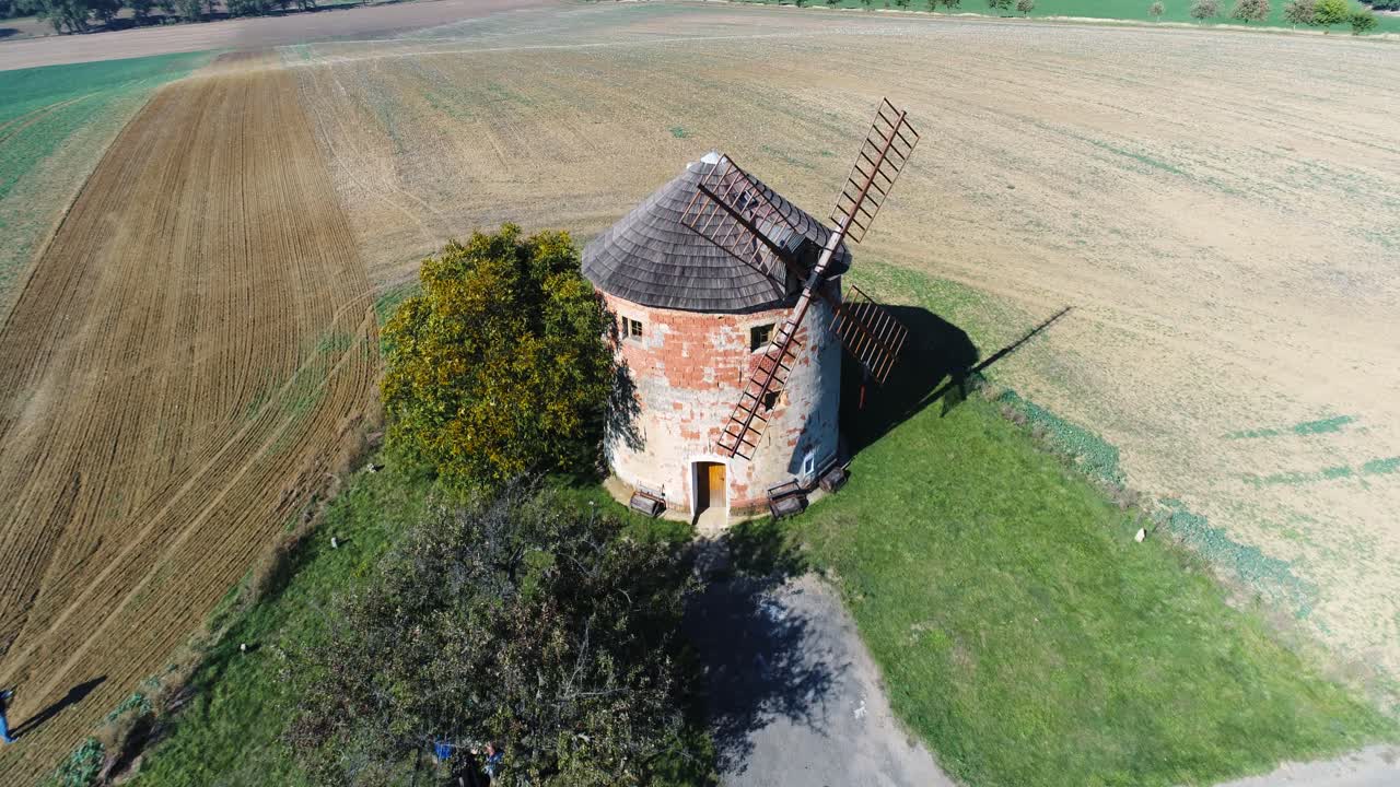 Drone flight over single windmill in the middle of fields with some people in front of it