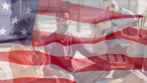 animation of waving flag of america over happy diverse friends socialising on sunny beach