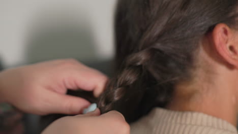 nanny gently braiding girl’s hair, focused caregiving moment, close-up of loving care, child relaxed, soft lighting, tender family connection, cozy indoor setting, affectionate bonding