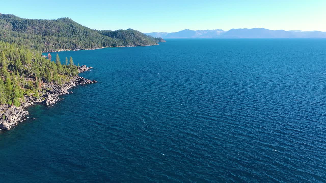 Aerial View Over Idyllic Lake Champlain In New York and Vermont with Clear Blue Water, Pine Tree Forest and Rip Rap Rocky Shoreline- drone shot