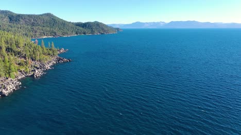 Aerial-View-Over-Idyllic-Lake-Champlain-In-New-York-and-Vermont-with-Clear-Blue-Water,-Pine-Tree-Forest-and-Rip-Rap-Rocky-Shoreline--drone-shot