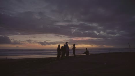 Gruppe-Von-Freunden,-Die-Am-Strand-An-Der-Küste-Von-Bali-Stehen-Und-Sich-Abends-Unterhalten
