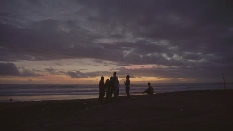 group of friends standing on beach on coast of bali chatting together in the evening