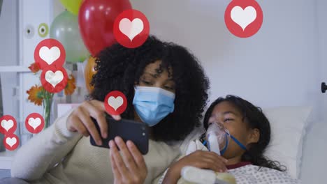 Animation-of-heart-icons-over-african-american-mother-and-daughter-with-face-masks-using-smartphone