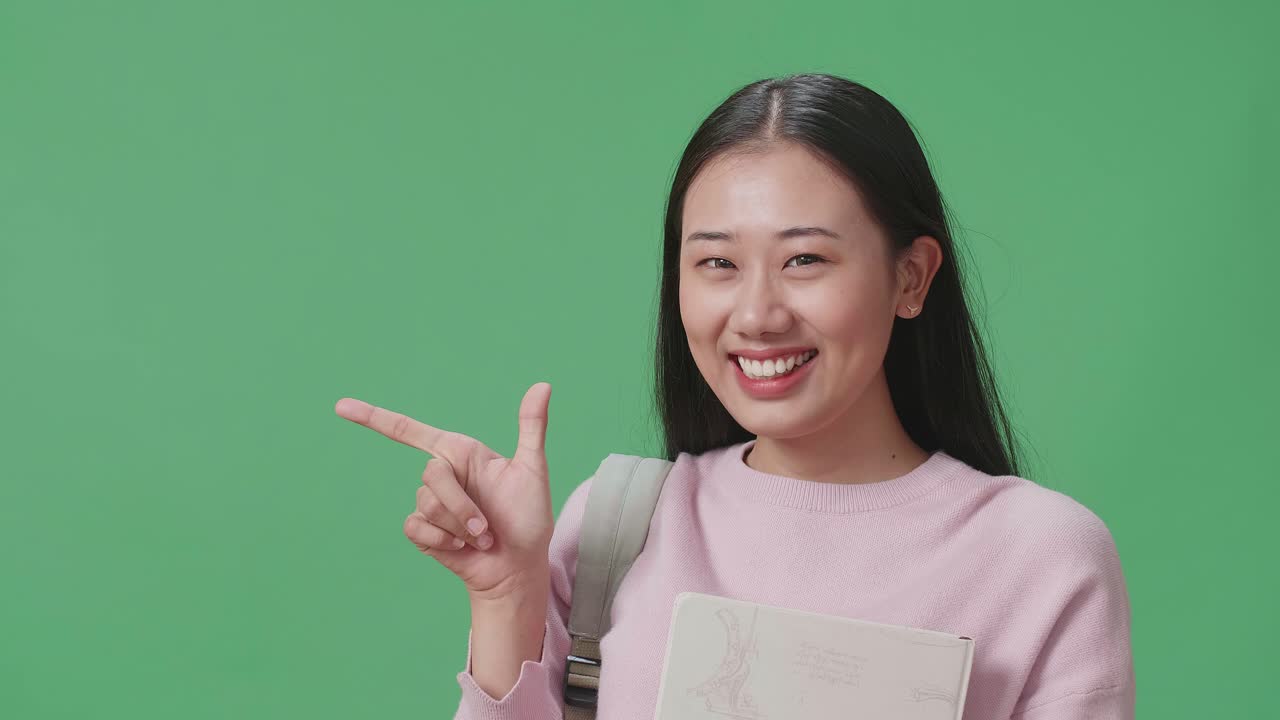 녹색 스크린 스튜디오에서 책과 직접 손가락을 들고 있는 아시아 여성 학생