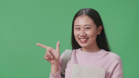 asian woman student holding book and direct fingers side on green screen studio