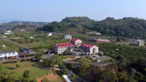 a large red-roofed building amidst green hills under clear skies, daylight, aerial view