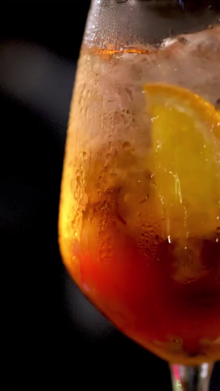 Primo piano di un cocktail Negroni mescolato con ghiaccio in un'illuminazione soffusa e suggestiva di un bar.