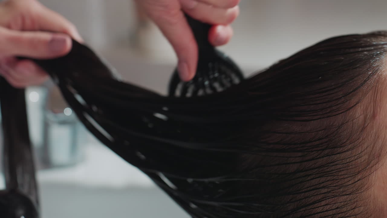 Pengaplikasian dari dekat kondisioner yang kaya ke sepanjang rambut basah di basin salon, stylist mendistribusikan produk dengan gerakan menyisir untuk memastikan cakupan merata dan tekstur halus, wastafel klinis dan diredam
