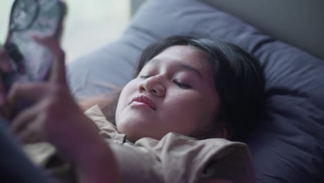 indonesian girl sitting by window, playing with her phone, enjoying a calm moment
