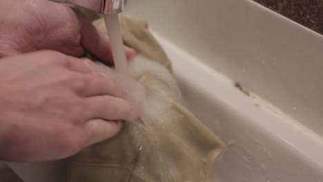 thoroughly washing of a beige clothing in a kitchen sink