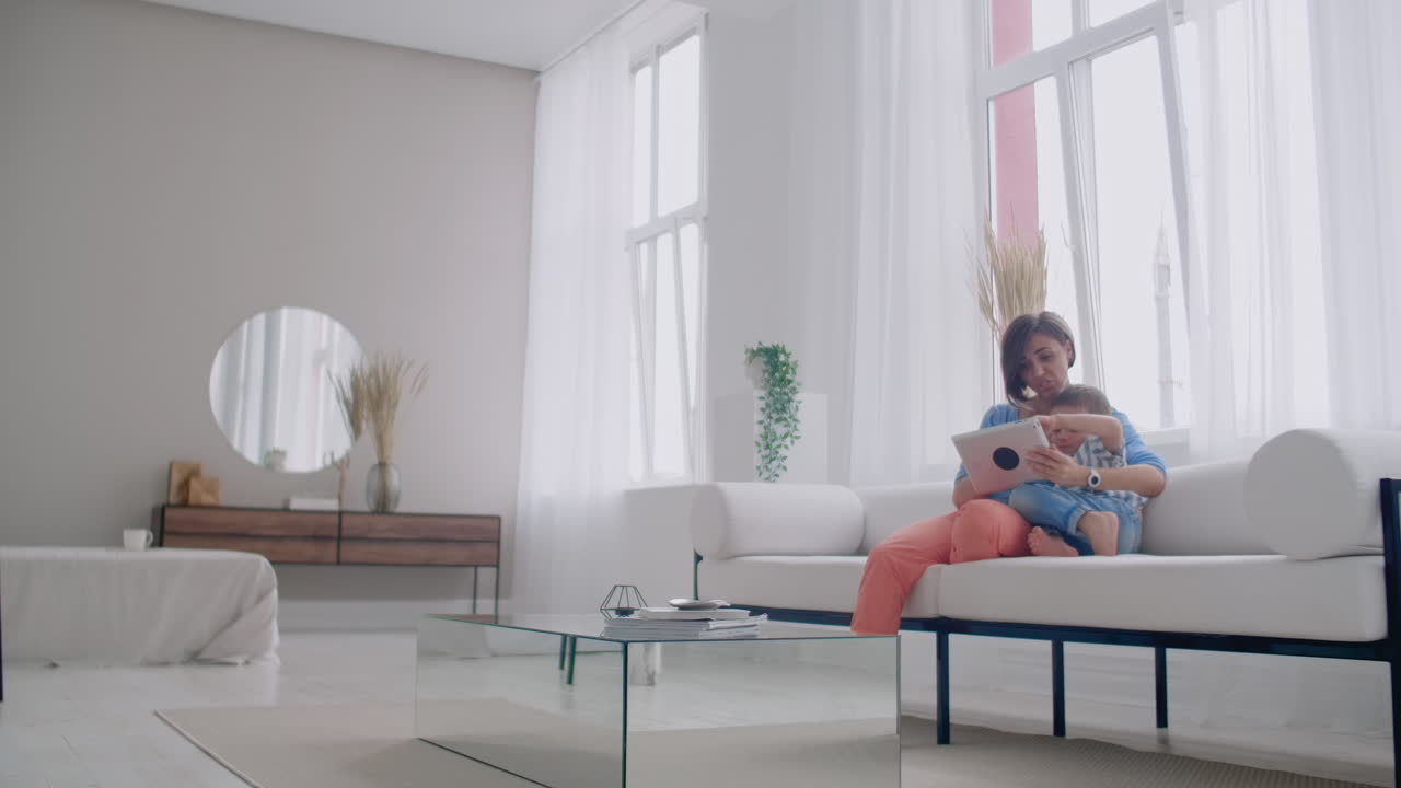 Happy family mom and kid son using digital tablet sitting on sofa smiling parent mother with child son holding pc computer looking at screen do online shopping make video call watch cartoons